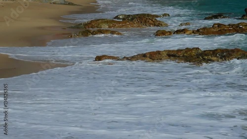 Beautiful white bubbles created on the beach by ocean waves on seashore. The ocean waves hit the rocks on the beach.