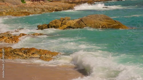 Beautiful white bubbles created on the beach by ocean waves on seashore. The ocean waves hit the rocks on the beach.