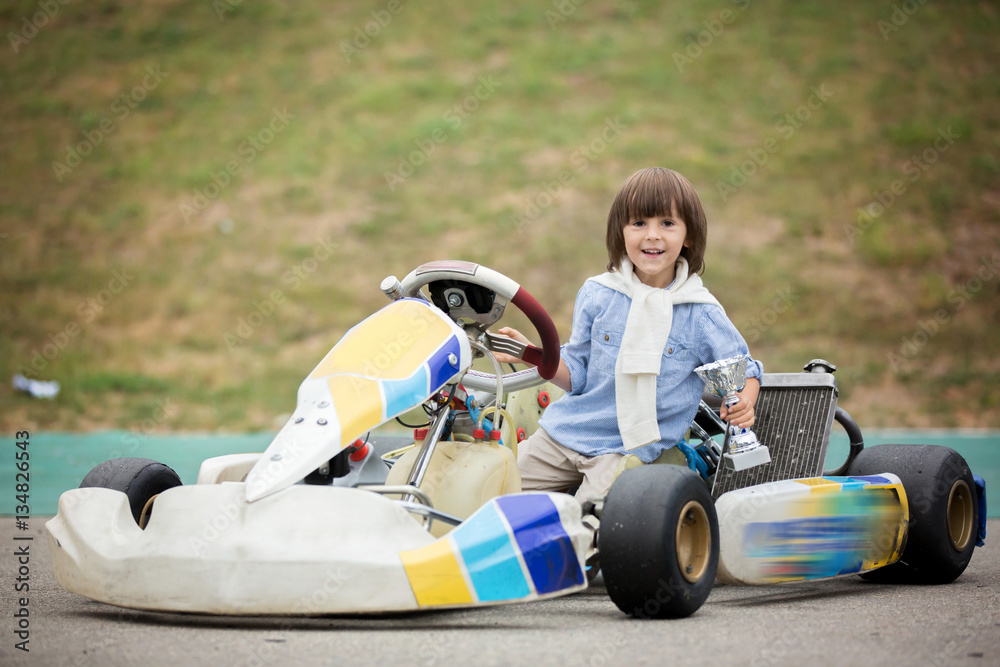 Cute child, riding go cart, wins champion cup, happiness winner concept Cute child, riding go cart, wins champion cup, happiness winner concept