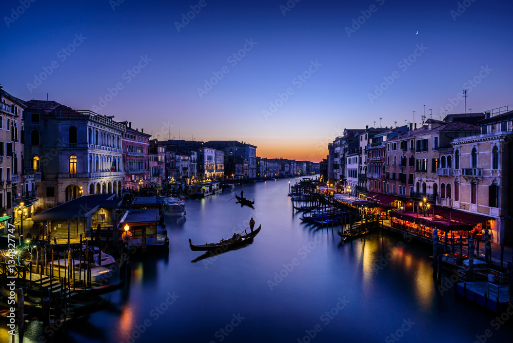 Long exposure of the Grand Canal seen from Rialto bridge at sunset. Gondolas seem resting on the water. The atmosphere is magical and surreal as Venice