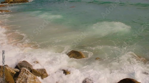 Beautiful white bubbles created on the beach by ocean waves on seashore. The ocean waves hit the rocks on the beach.