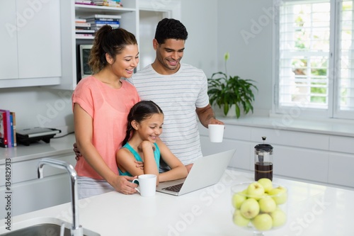 Parents and daughter using laptop in kitchen at home