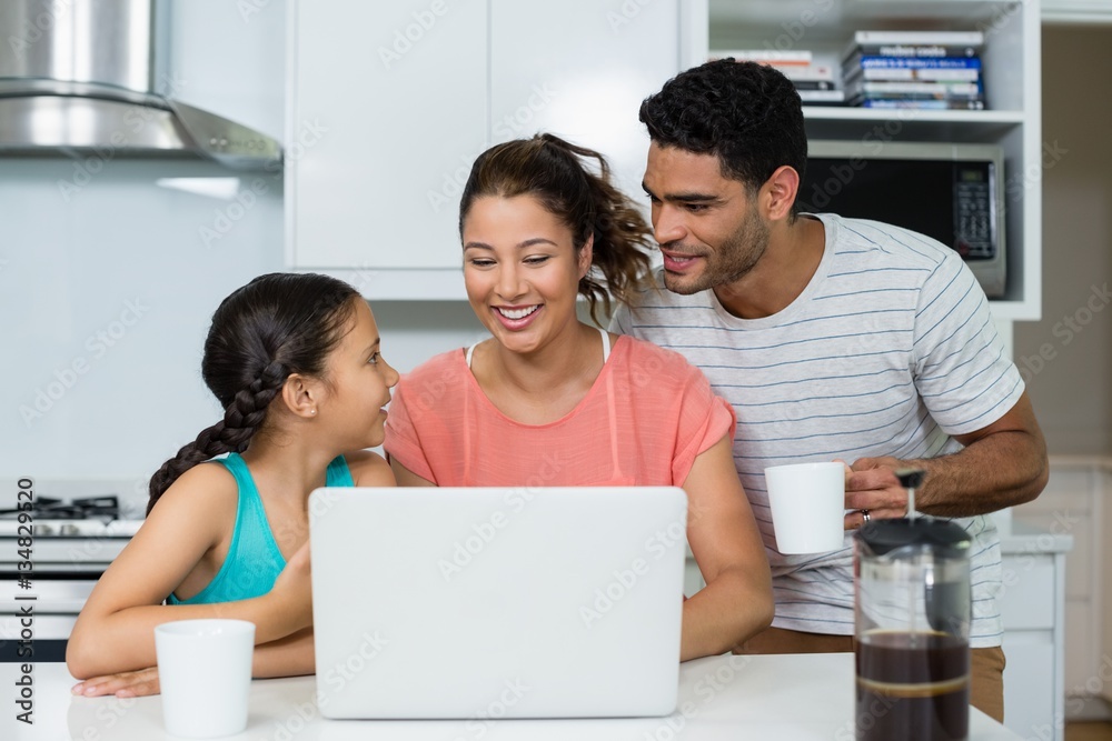 Parents and daughter using laptop in kitchen at home Parents and daughter using laptop in kitchen at home