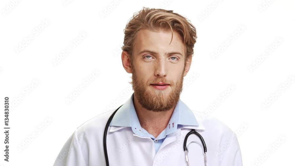 Confident Caucasian male doctor with light beard wearing medical overall showing ok with fingers on white background in slowmotion