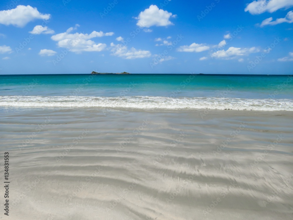 View of Pigeon Island over Beautiful White Sand Beach with patterns and  turquoise water Beach breaking waves with Blue Sky with White clouds