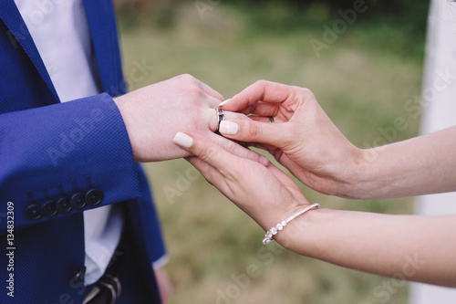 Wedding vow tradition. Closeup of a bride putting a modern gold wedding ring onto the groom's finger.