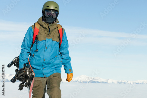 Snowboarder holding snowboard in hand and walking at the top of a mountain