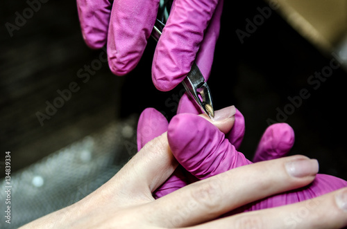 The process of removing the cuticles using tweezers for manicure. Hands Wizard reserved gloves.