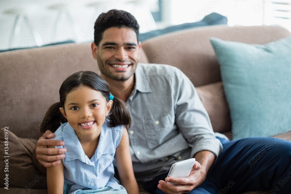 Portrait of father and daughter sitting on sofa in living room