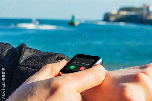  Close up of man's hands wearing smartwach with incoming call on the screen.