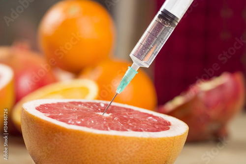 Needle and syringe injected in the fruit. Nutrition concept. Enhanced fruits. GMO. Healthy life versus unhealthy life. Fruits and pills on the table.
