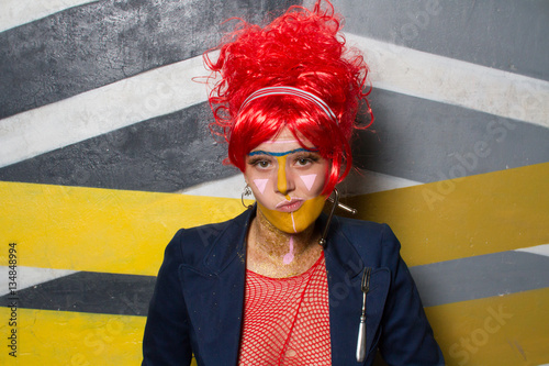 Retrato de chica joven con estética punk y post-punk (tribu urbana futurista) con peluca roja y con la cara pintada haciendo gestos provocativos