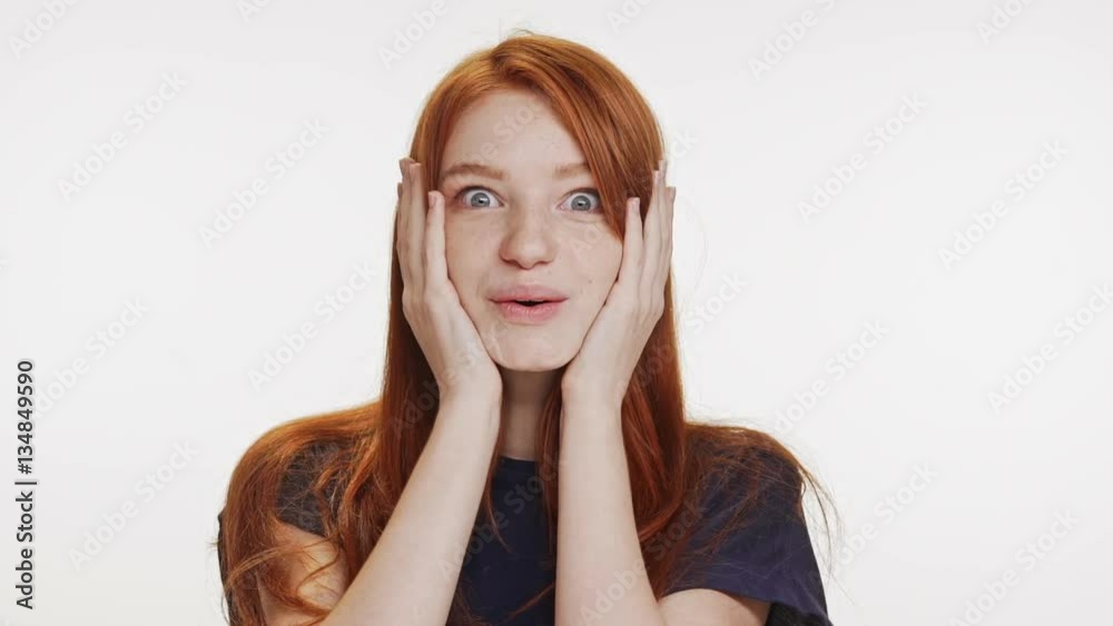 Young cute redhead teenage girl looking at camera in great amazement and holding head with hands on white background in slwomotion Young cute redhead teenage girl looking at camera in great amazement and holding head with hands on white background in slwomotion