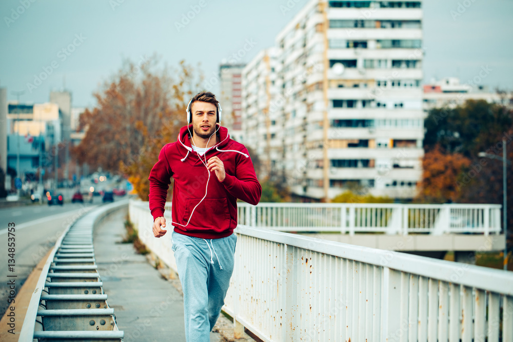 Fototapeta premium Man in red hoodie jogging beside the road in the city