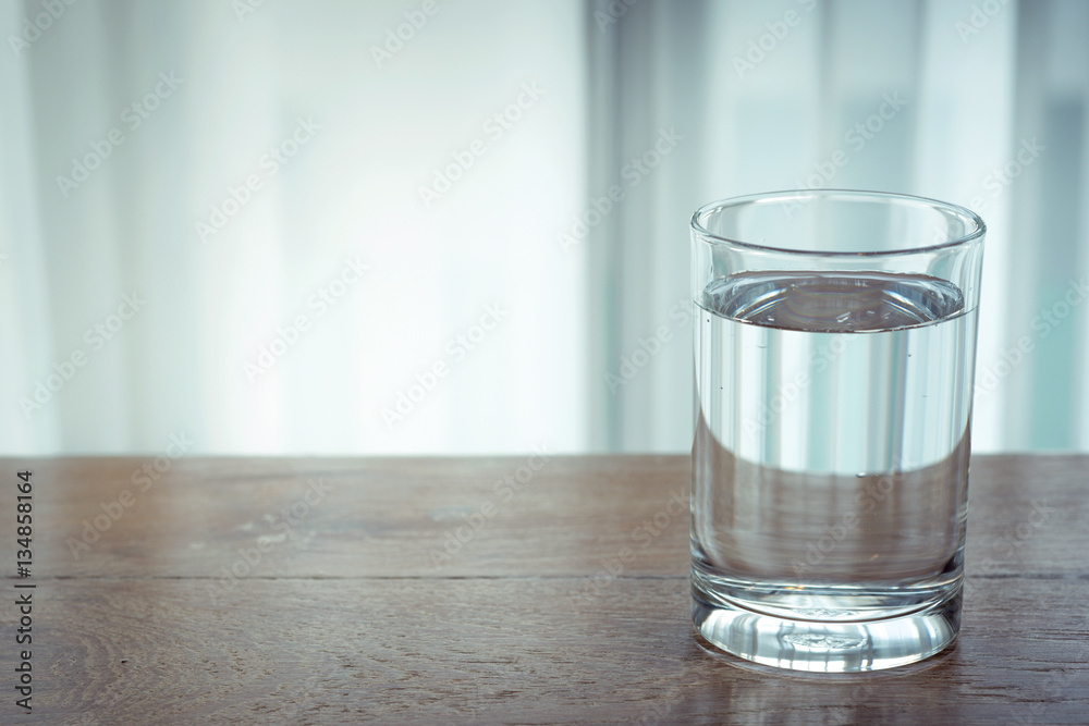 Glass of water on wooden table and light blurred background. Glass of water on wooden table and light blurred background.