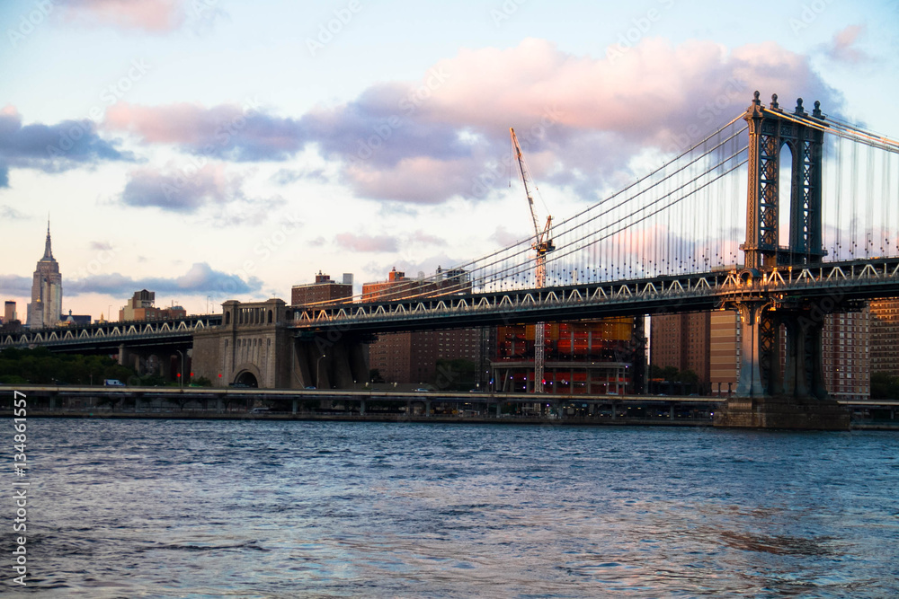 Manhattan bridge over the river and buildings in Manhattan with cloudy sky before sunset