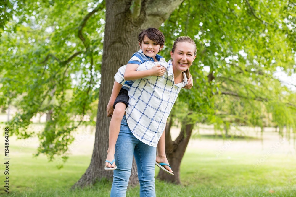 Fototapeta premium Mother giving a piggyback ride to his son in park
