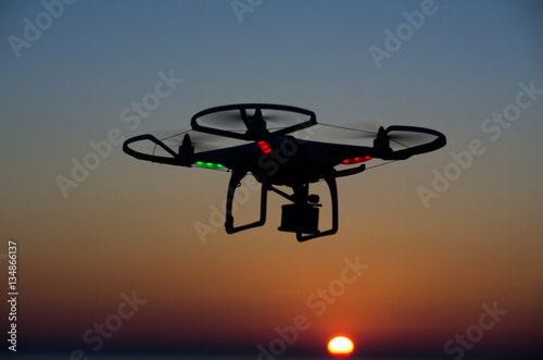 Flying drone with camera on the sky at sunset