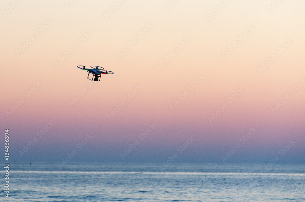 Flying drone with camera on the sky at sunset