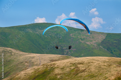 Paragliding in the sky. Two paraglider fly over the tops of the mountains in summer sunny day. Carpathians, Ukraine.