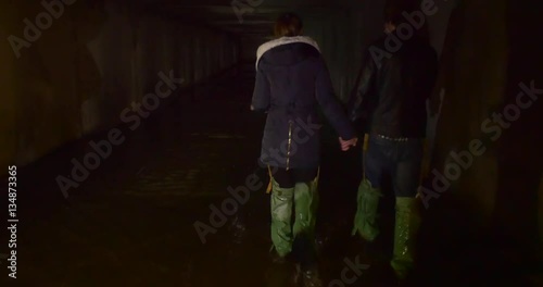 a Young Couple in Chemsuit Boots go Along a Tunnel, Which is Full of Dirty Dark Drain Waters in Kiev photo