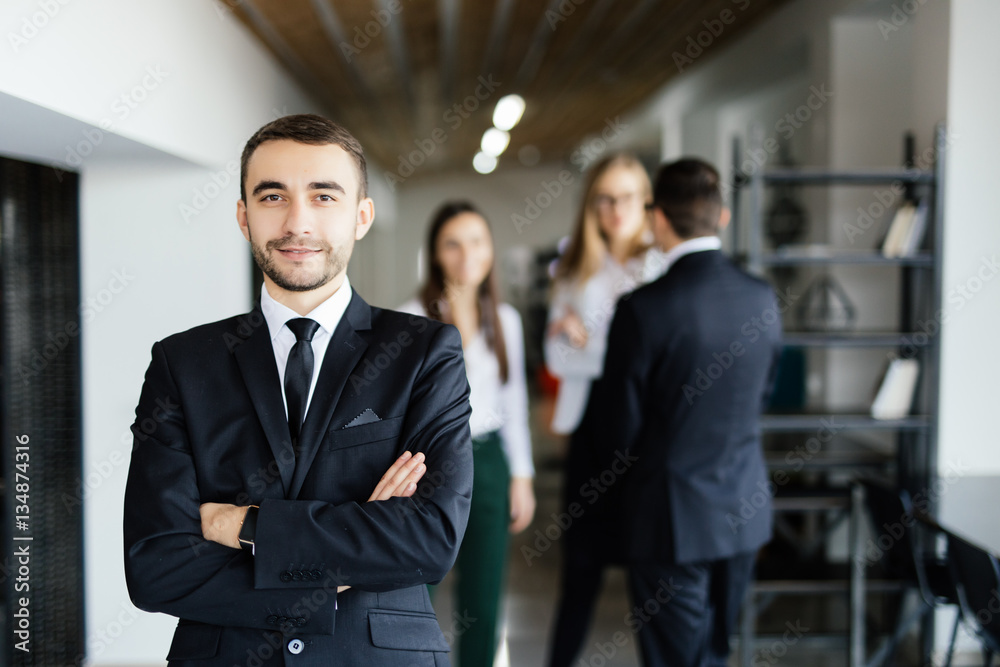 Young manager in front of his coworkers with crossed hands in modern office. Young manager in front of his coworkers with crossed hands in modern office.
