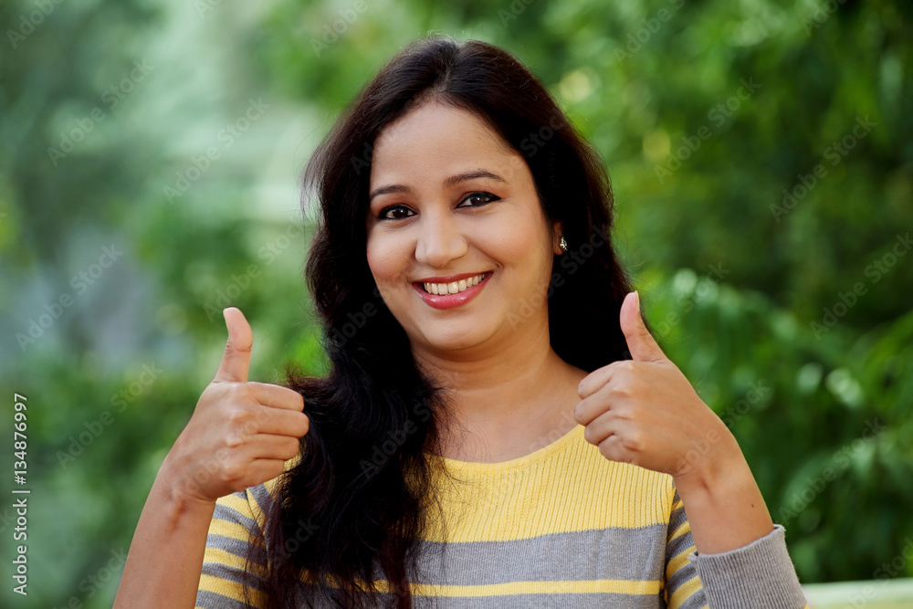 Smiling young woman making thumb up gesture at outdoors Smiling young woman making thumb up gesture at outdoors