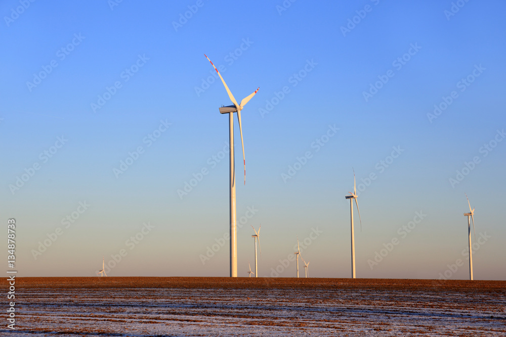 Elektrownie wiatrowe na ośnieżonym polu o zachodzie słońca.