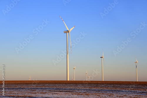 Elektrownie wiatrowe na ośnieżonym polu o zachodzie słońca.