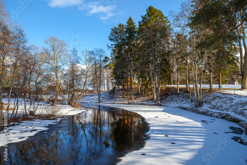 Winter icy river turn. Coasts with pine trees and wooden houses, little Estonian village