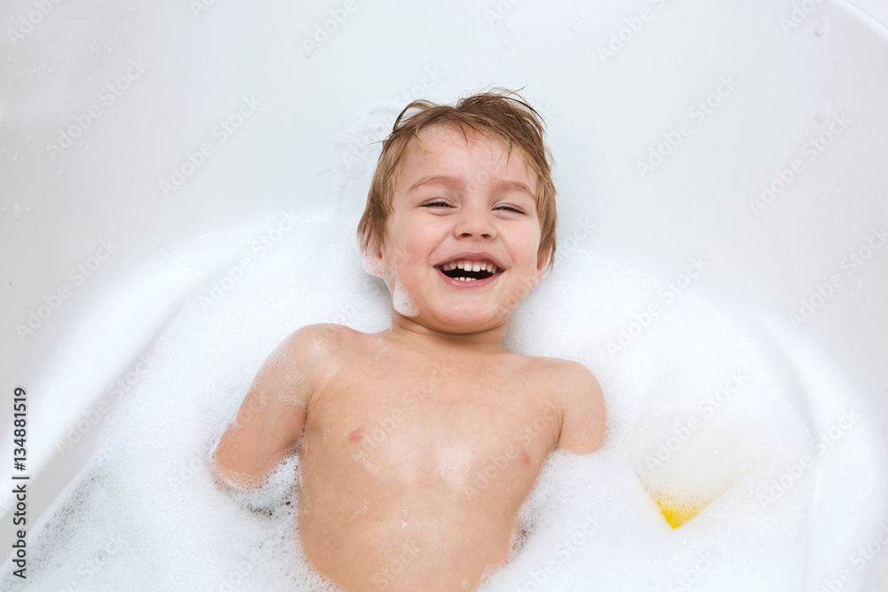 Funny child playing with water and foam in a bathroom. little boy bathes.