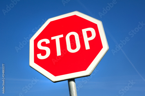 Stop traffic sign. Red octagon with white letters. Clear blue sky is behind road sign.
