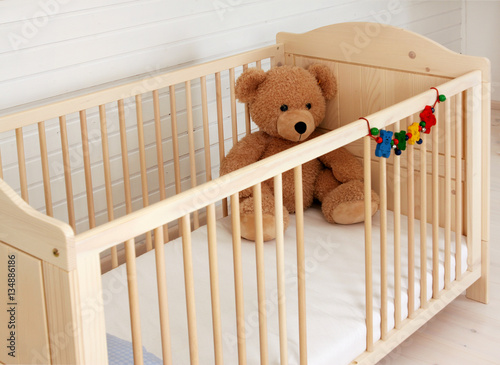 Ein Teddybär sitzt in einem Kinderbett