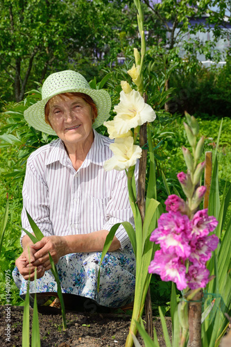 Older woman smiling on a bed with white and purple gladioli.