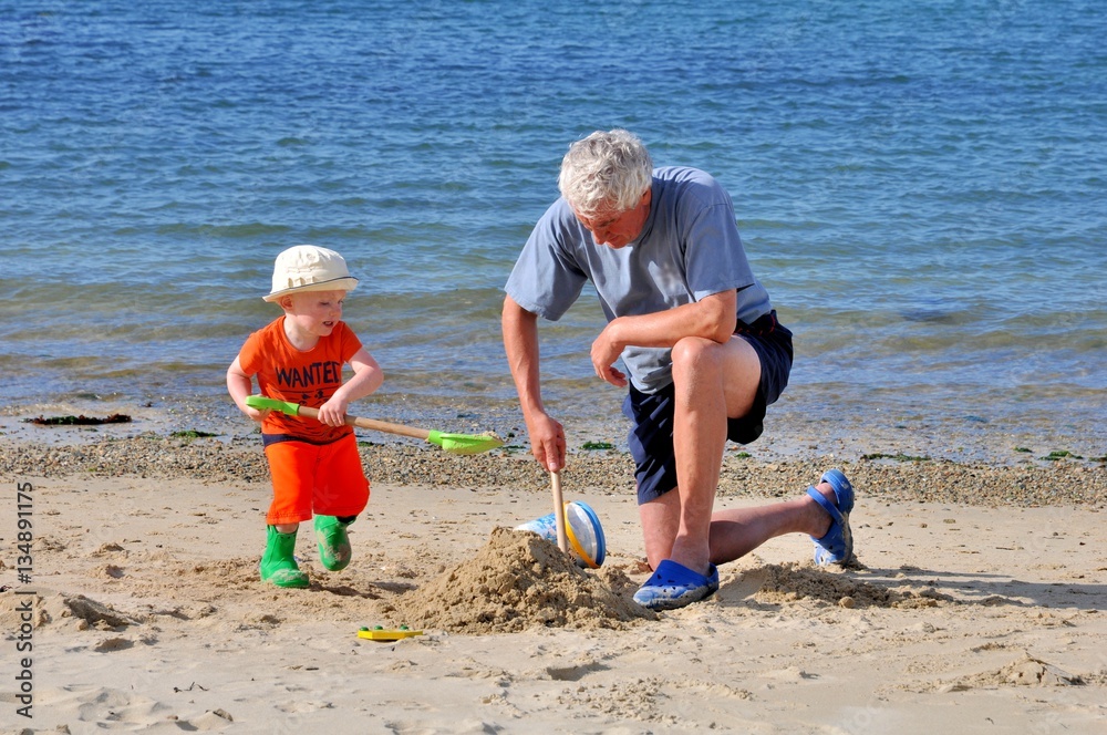 Un petit garçon et son grand-père jouent dans le sable sur une plage en Bretagne Un petit garçon et son grand-père jouent dans le sable sur une plage en Bretagne