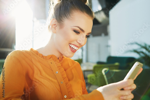 Young woman laughing while texting on her phone in a cafe