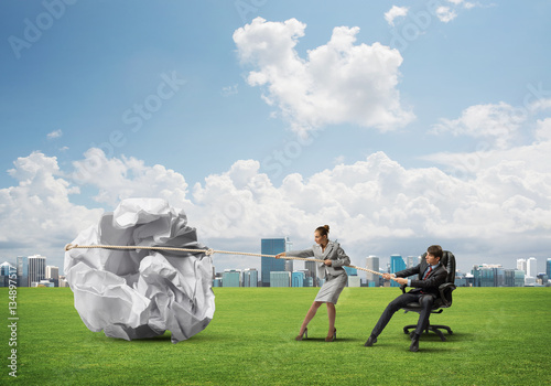 Businesspeople pulling with effort big crumpled ball of paper as creativity sign photo