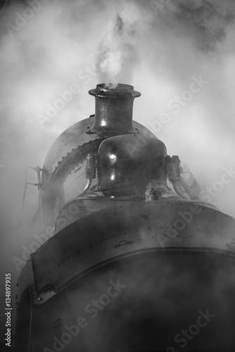 Restored Victorian era steam train engine with full steam in bla