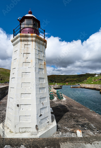 Lybster, Scotland - June 4, 2012: Closeup of the lighthouse at Lybster harbor. Harbor, blue North Sea water, green hills, dark stone pier and lobster traps in background. photo