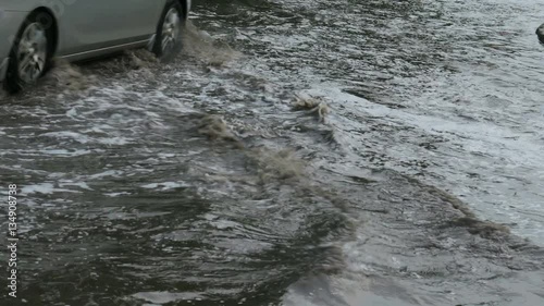 Flooded road cars moving slowly in deep puddles.