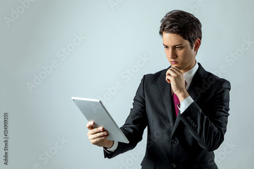 young businessman holding tablet PC and thinking something on white background