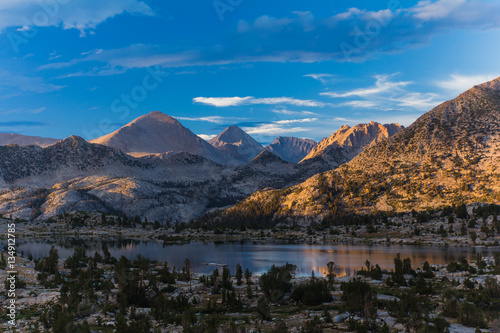 Sunset over an alpine basin with lake and pine trees surrounded by tall bare granite peaks in California