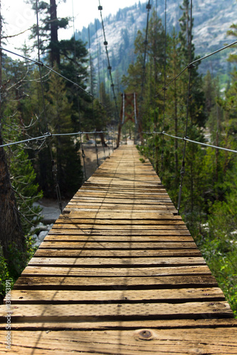 An old wooden suspension bridge with broken slats hangs over a river near the Rae Lakes in California s high sierra