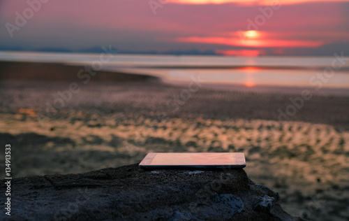 Fotografija forgot gadget, tablet, thrown on the rock on sunset background.