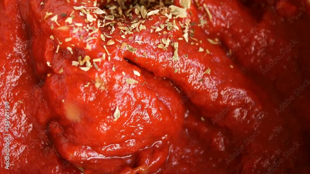 Macro of pouring oregano on tomato puree and mixing it with spoon. Macro of pouring oregano on tomato puree and mixing it with spoon.