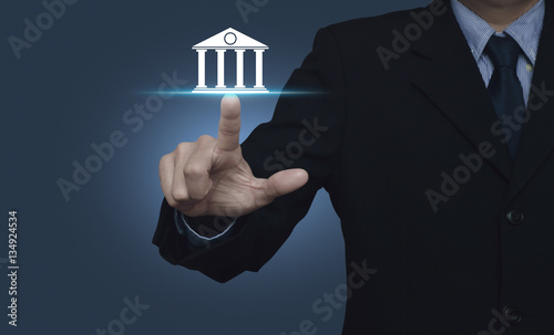 Businessman pressing bank icon over blue background, Business banking concept