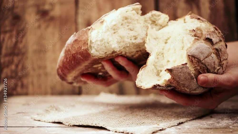 Female baker hands breaking homemade bread over wooden background.