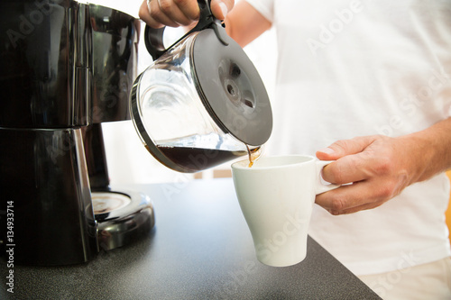 Photo Man in the kitchen pouring a mug of hot filtered coffee from a glass pot