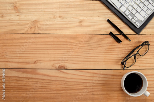 Office desk table with keyboard, notebook, pen, cup of coffee and flower. Top view with copy space (selective focus)