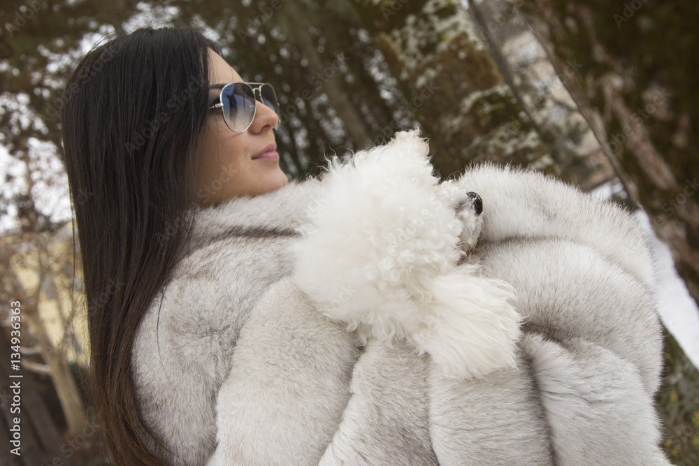 Beautiful winter close-up of a young woman in the winter snowy scenery. Woman wearing a white fur coat. Playing with the dog at the park. Beautiful winter close-up of a young woman in the winter snowy scenery. Woman wearing a white fur coat. Playing with the dog at the park.
